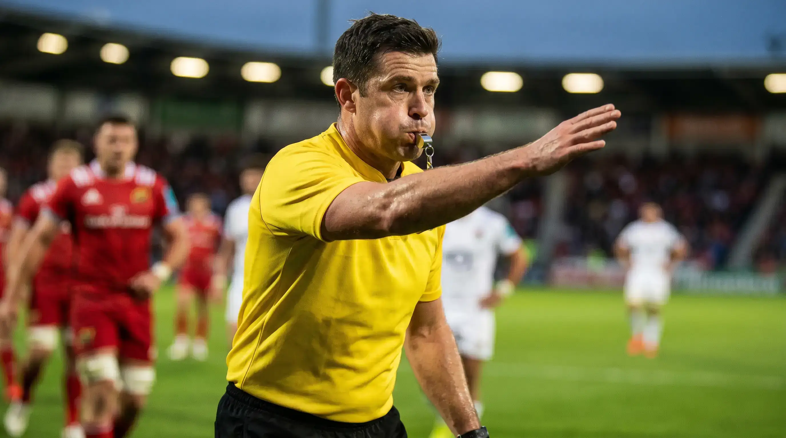 Rugby referee blowing a whistle during an international Test match under stadium lights