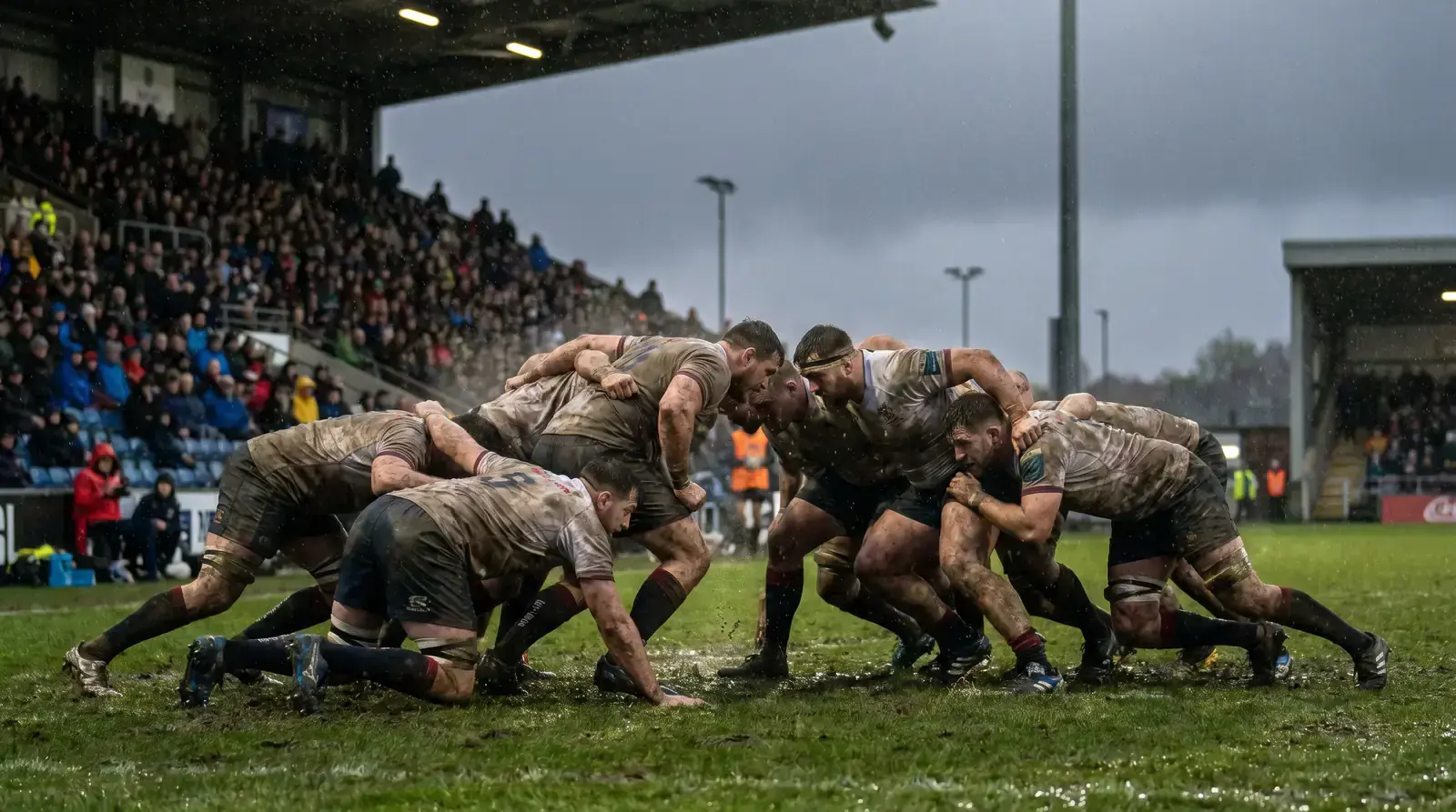 Rugby players contesting a scrum in heavy rain on a sodden pitch